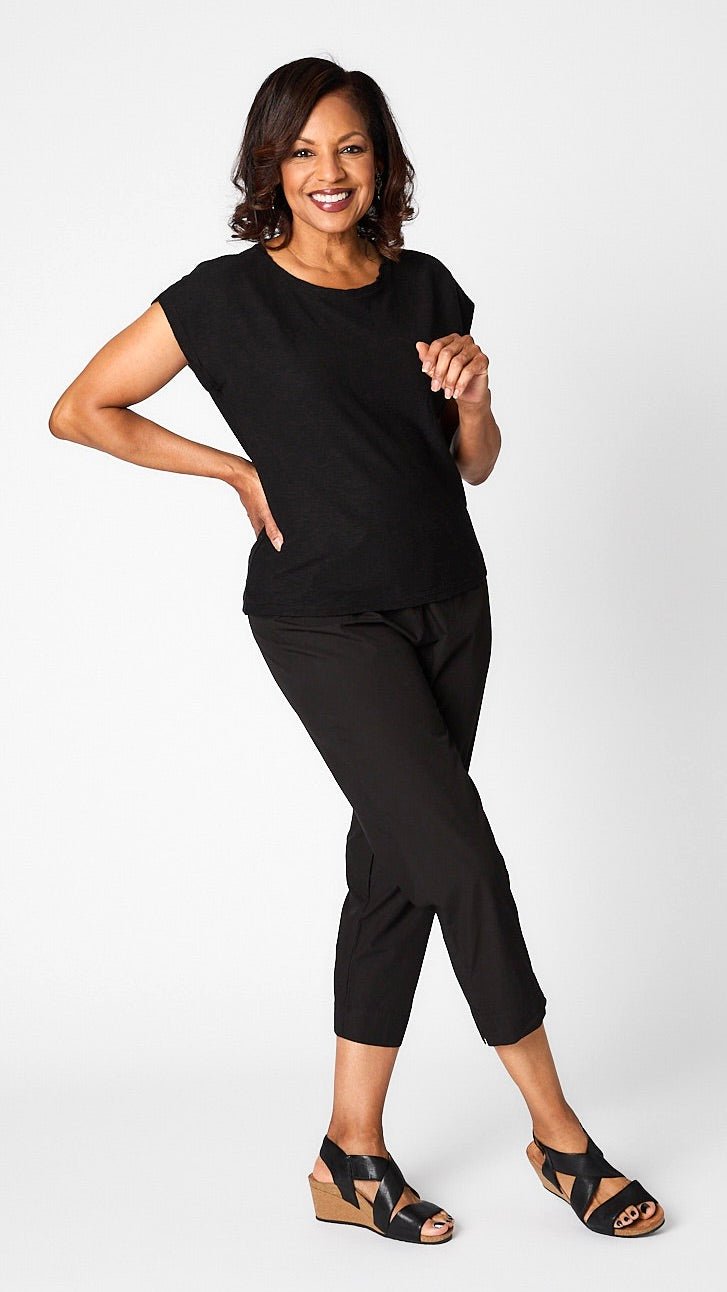 Model posing in black cropped sleeve box top, black tapered cropped pants in organic poplin, and black leather wedge sandals.