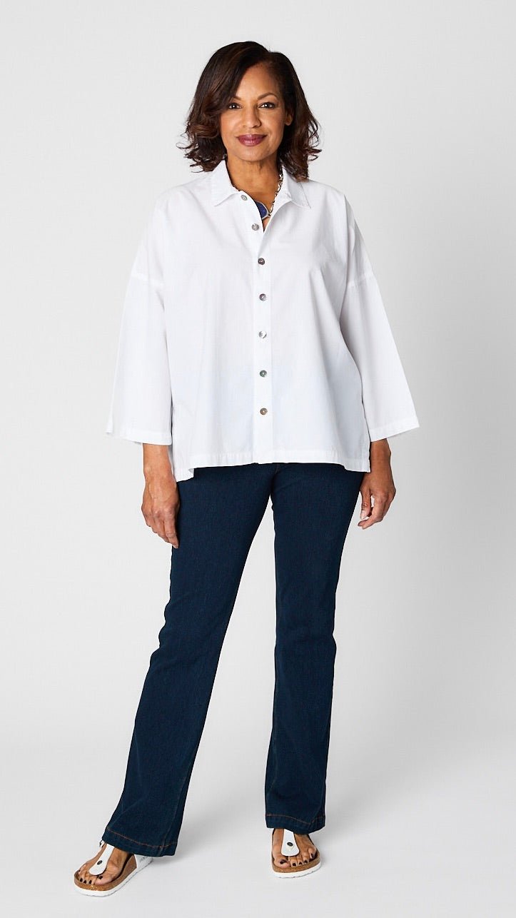 Model wearing white boxy button up, indigo bootcut denim jeans, lapis pendant necklace, and white sandals.