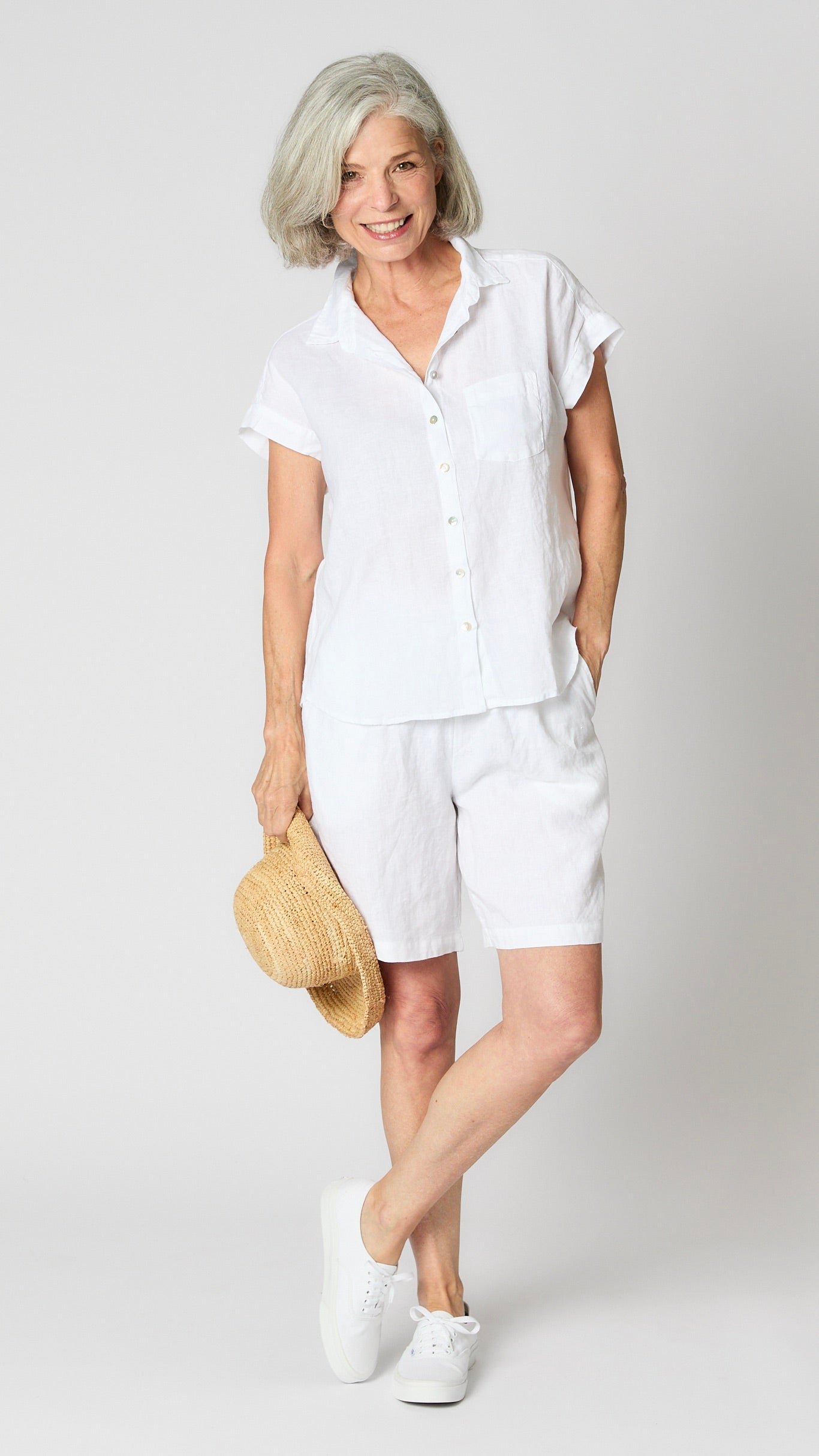Model wearing white linen short sleeve linen button-up top, white linen shorts, and white canvas sneakers.
