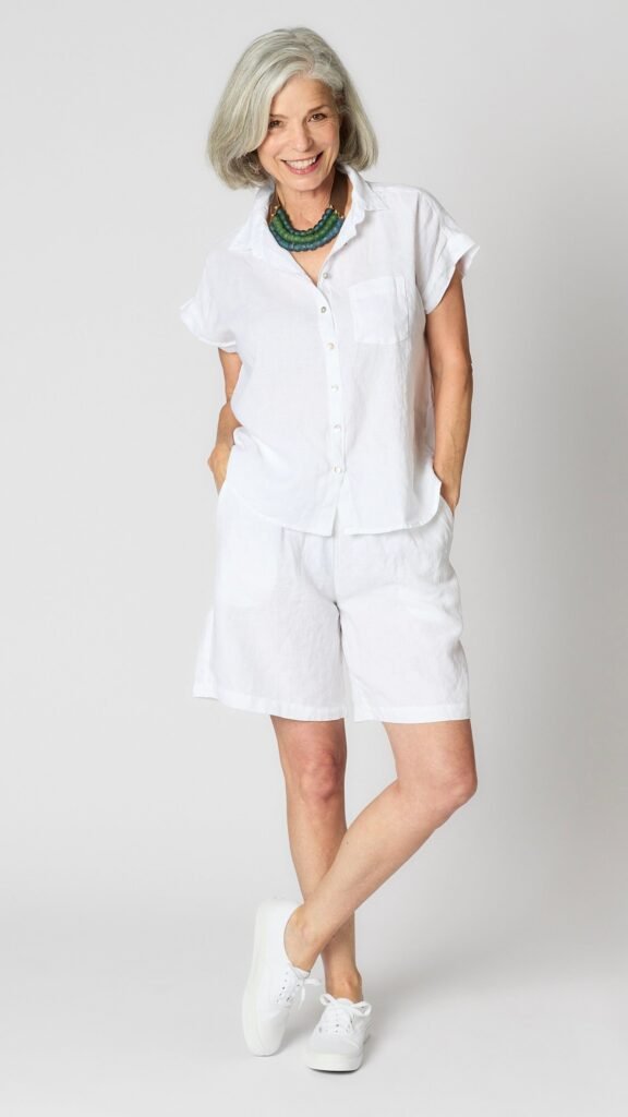 Model wearing white linen short sleeve linen button-up top, white linen shorts, and white canvas sneakers.