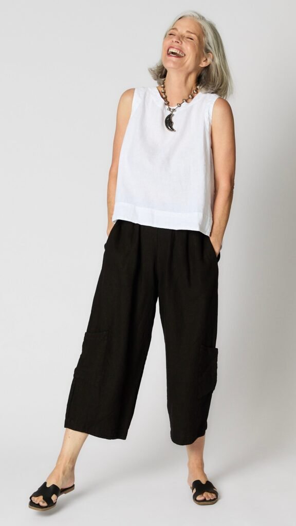 Model wearing white linen sleeveless tank with hi-lo silhouette, and black cropped linen pants with patch pockets.