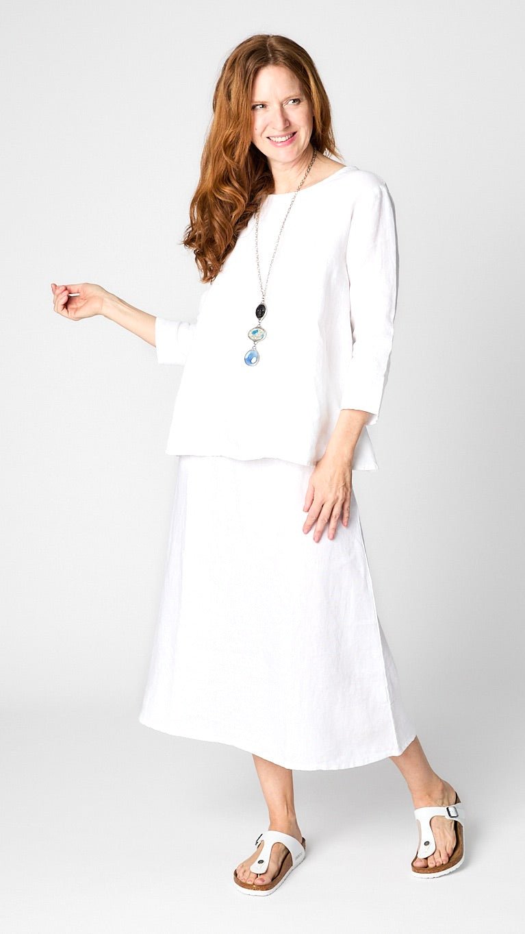 Model wearing white linen 3/4 sleeve shirt with A-line silhouette, white A-Line Linen skirt, triple stone pendant necklace, and leather sandals.