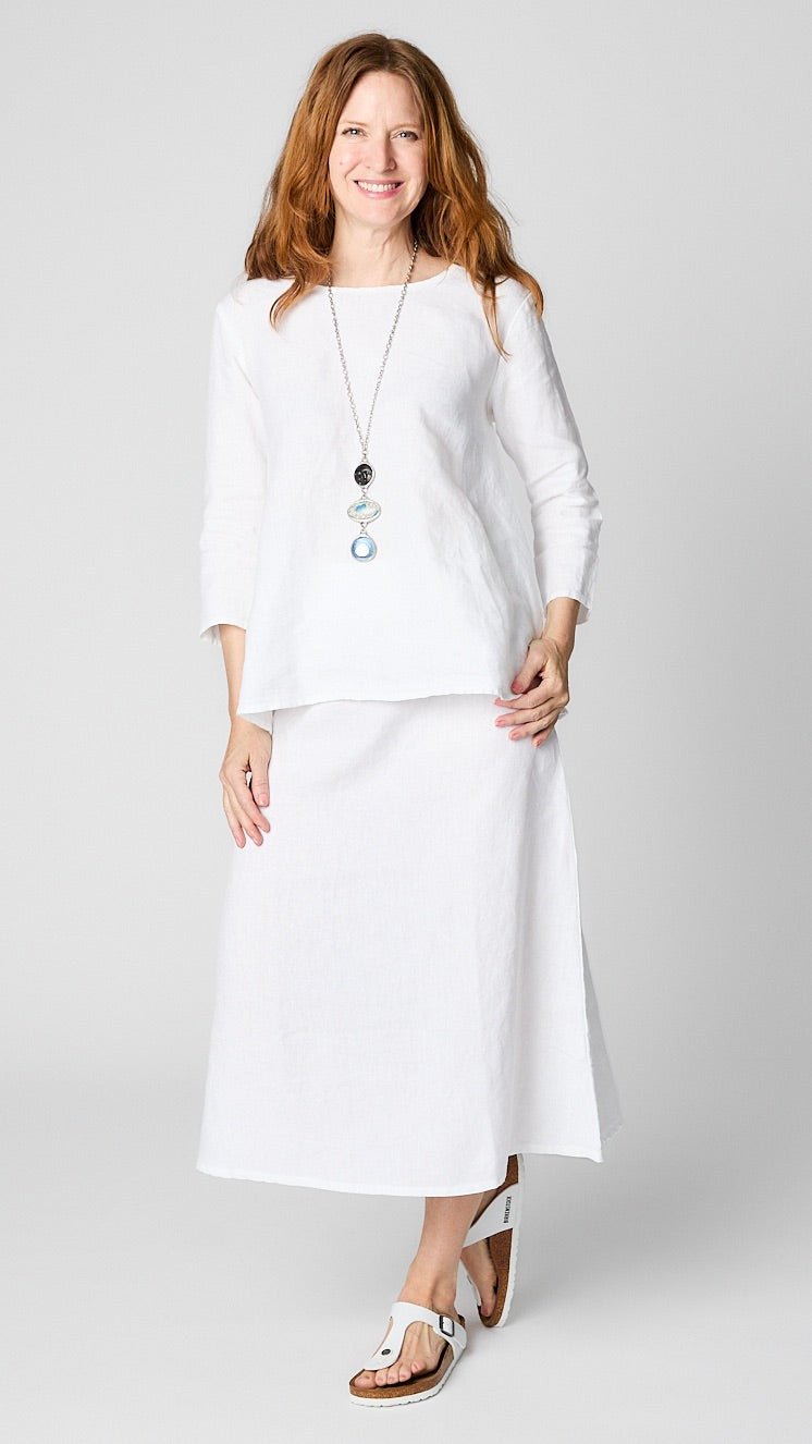 Model wearing white linen 3/4 sleeve shirt with A-line silhouette, white A-Line Linen skirt, triple stone pendant necklace, and leather sandals.