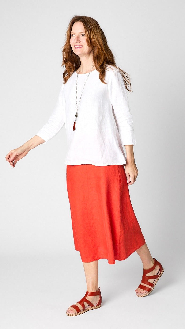 Model wearing white linen 3/4 sleeve shirt with A-line silhouette, “tabasco” orange A-Line Linen skirt, coin pendant necklace, and leather sandals.