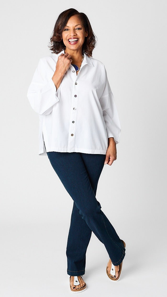 Model wearing "chalk" white button-up top with relaxed hemline and 3/4 sleeves over indigo baby bootcut jeans and white sandals.