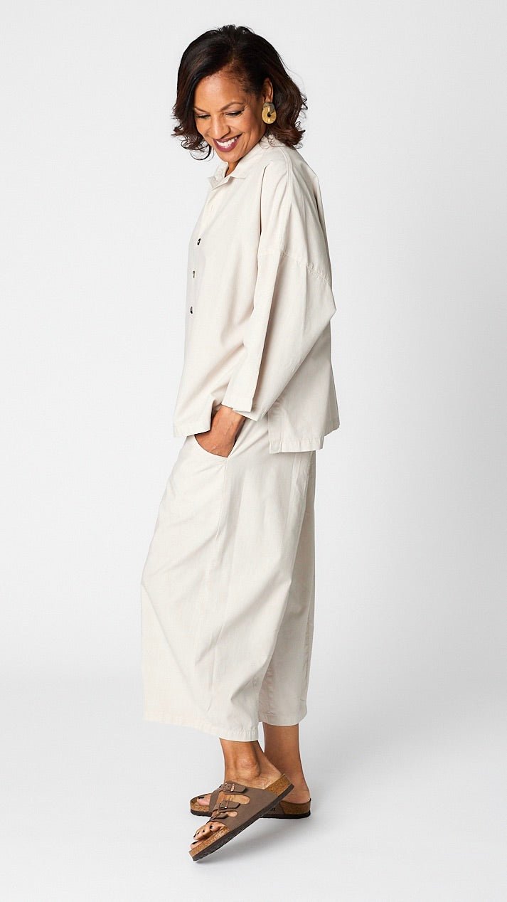 Model wearing cloud button-up top with relaxed hemline and 3/4 sleeves over cloud cropped one pocket pants and brown sandals.